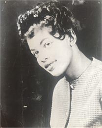 Black and white photo of a young black woman with curly hair smiling at the camera.