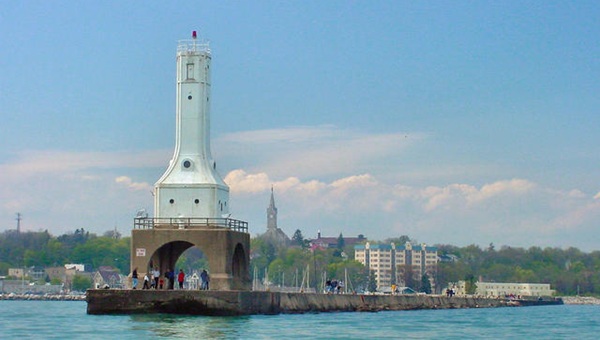 A white pier light station overlooks the water with people on the pier underneath