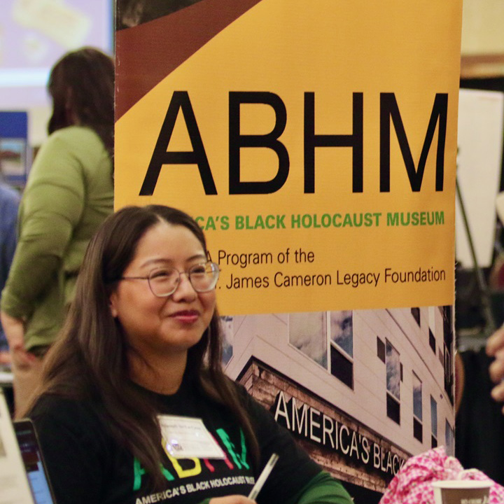 A representative from America's Black Holocaust Museum sits at a table with a banner representing the museum behind her