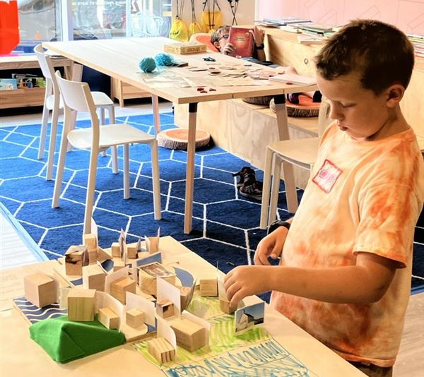A young boy playing with wooden blocks and paper on a table at the History Maker Space