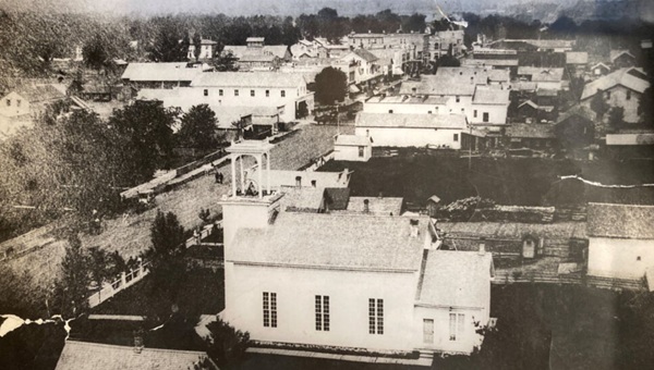 Black and white photo of the main street of a town including a white church in the foreground