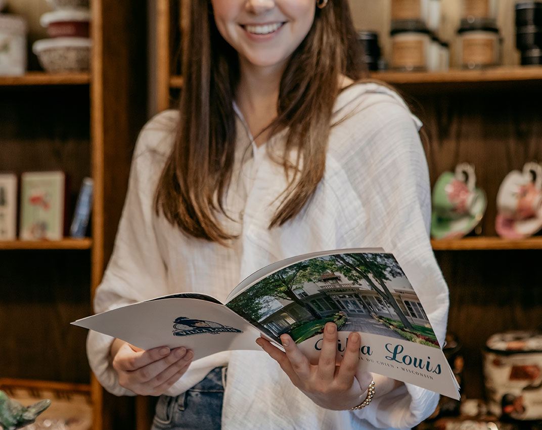 A light-complected woman with brown hair smiles and looks at a magazine about Villa Louis