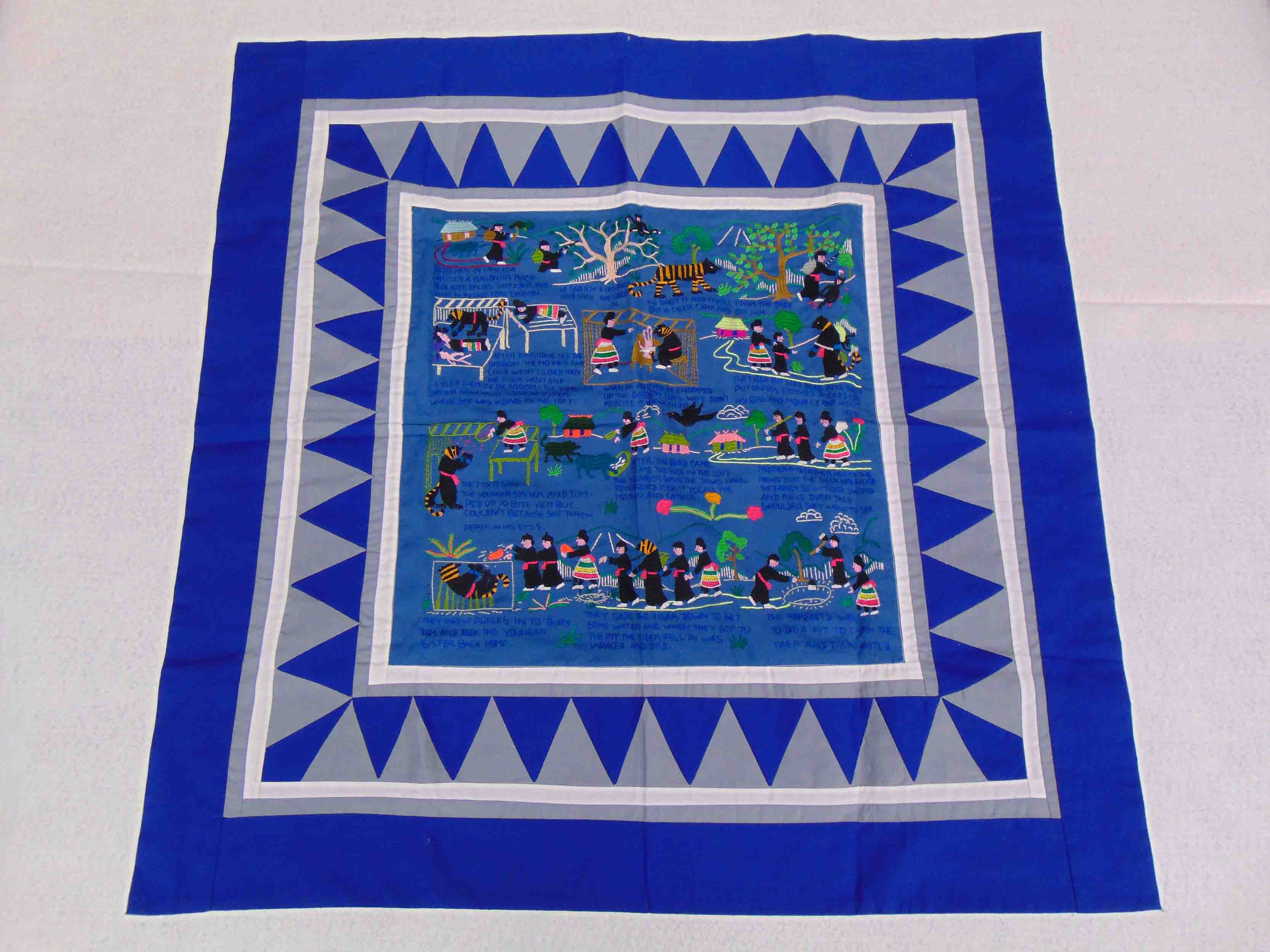 A blue tapestry with traditional embroidery depicting the Hmong refugee migration from their homeland to the United States.