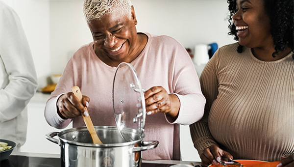 Two women laugh together as one stirs a pot.