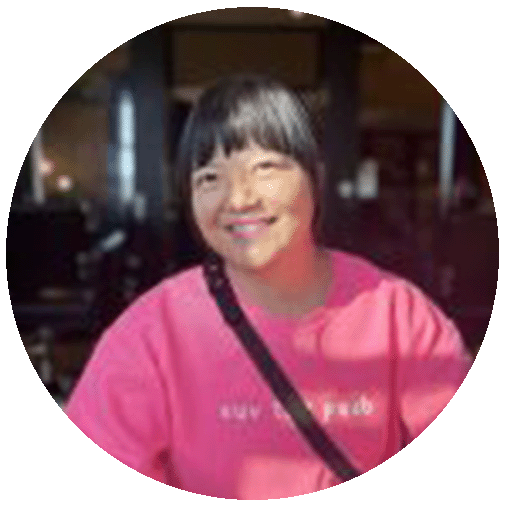 A woman with short black hair wearing a pink sweatshirt smiling at the camera.