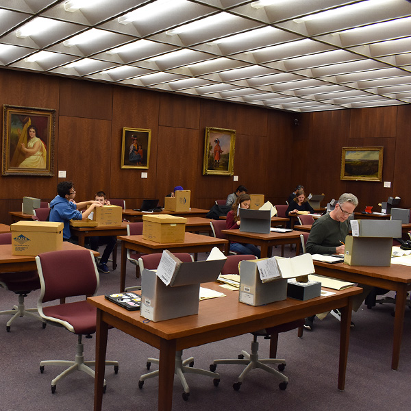 Researchers sit in the archives reading room looking through boxes of archival materials