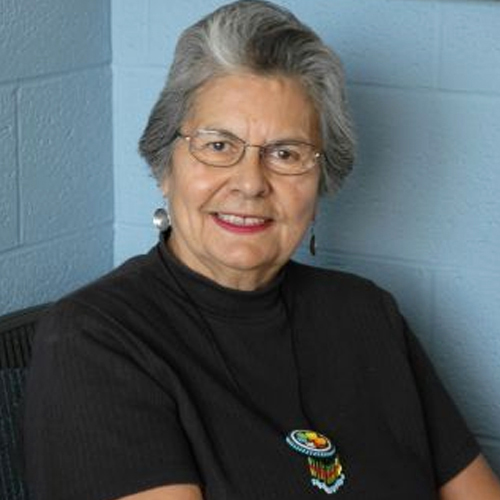 Ada Deer, 2007. A middle aged woman looking confidently at the camera while smiling. Her shirt is black and she wears beaded necklace pendant.