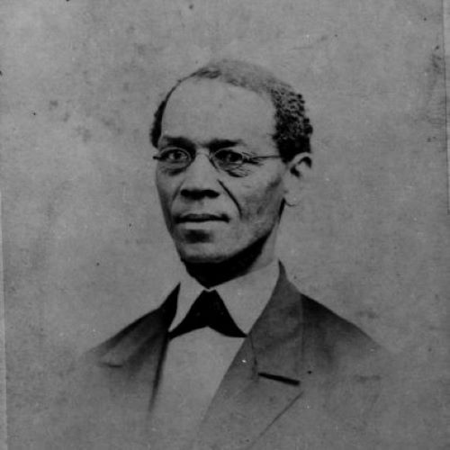 Head and shoulders portrait of Ezekiel Gillespie. He looks slightly to the left away from the camera, looking serious and austere. A small pair of spectacles sit on his nose and he wears a smart suit in this grainy old studio portrait