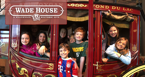 Wade House. A group of kids jammed into an old carriage at Wade House smile at the camera.